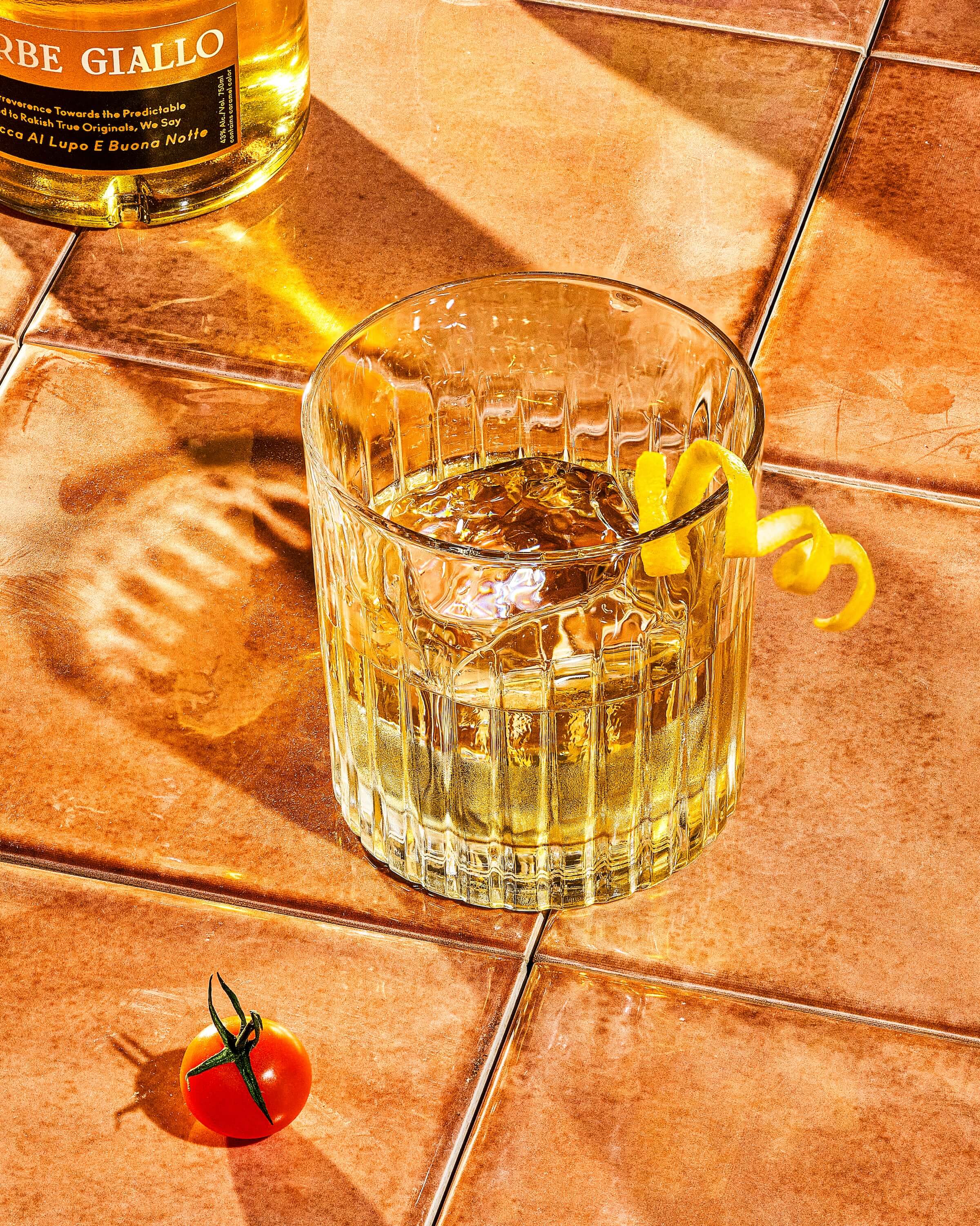 Glass with lemon peel  and Faccia Brutto Centerbe Giallo bottle on terra cotta tile