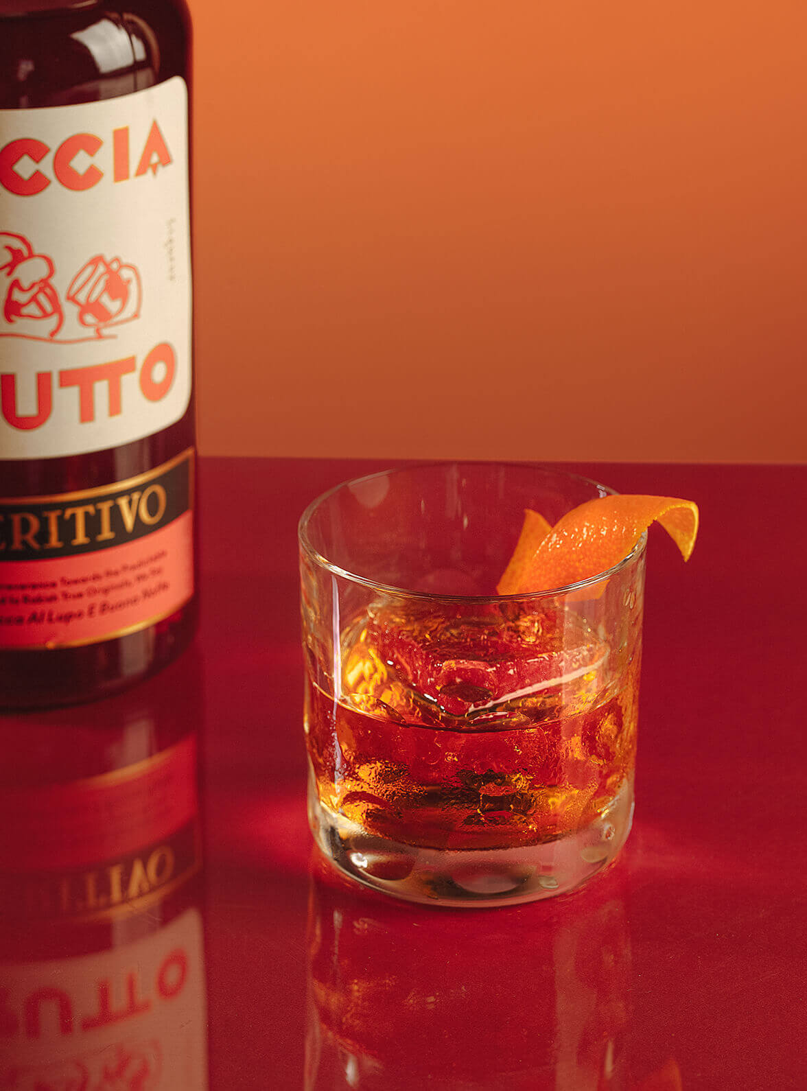 Cocktail on the rocks with orange peel and bottle of Faccia Brutto Aperitivo