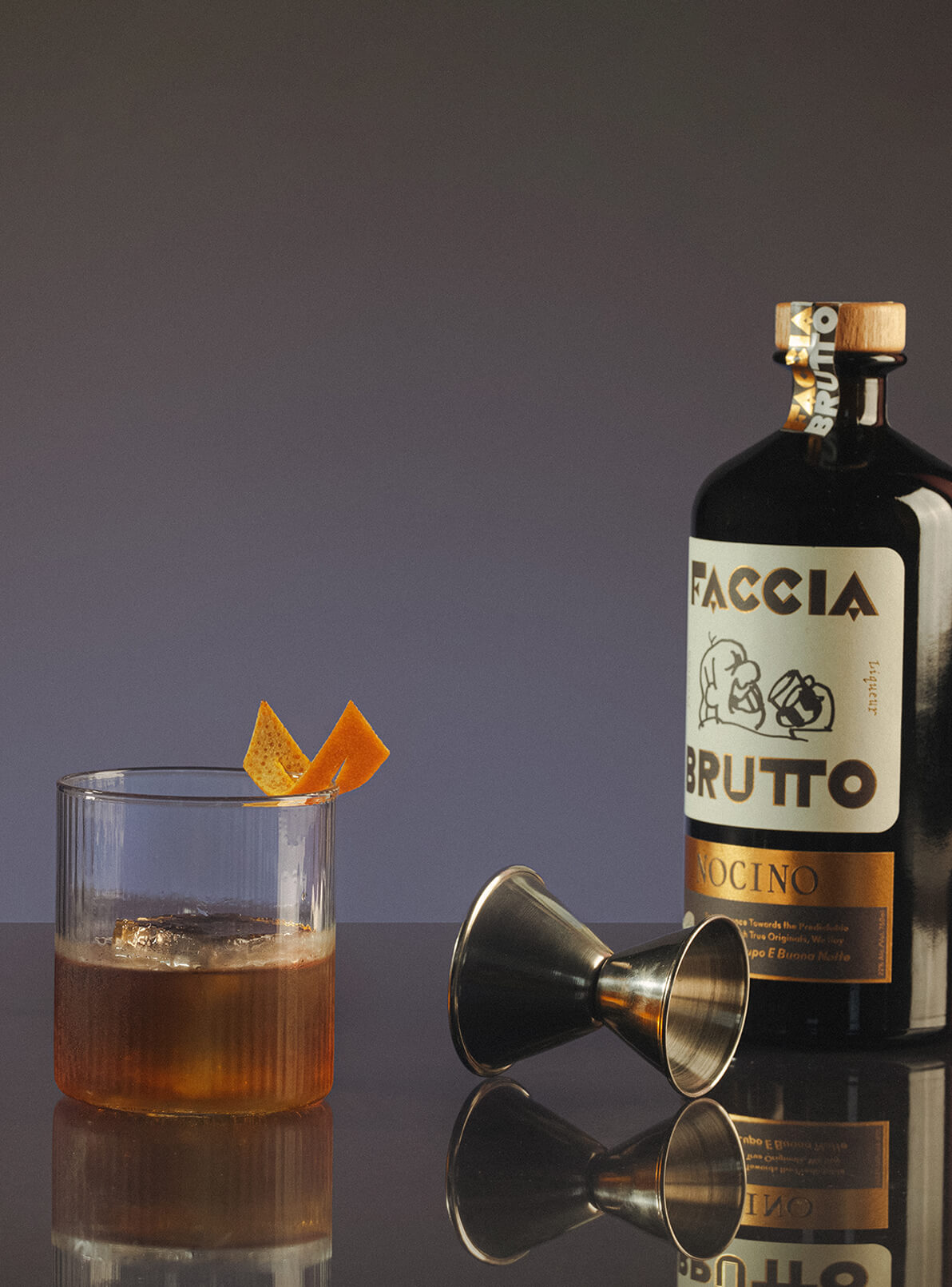 Cocktail with orange peel, jigger and bottle of Faccia Brutto Nocino