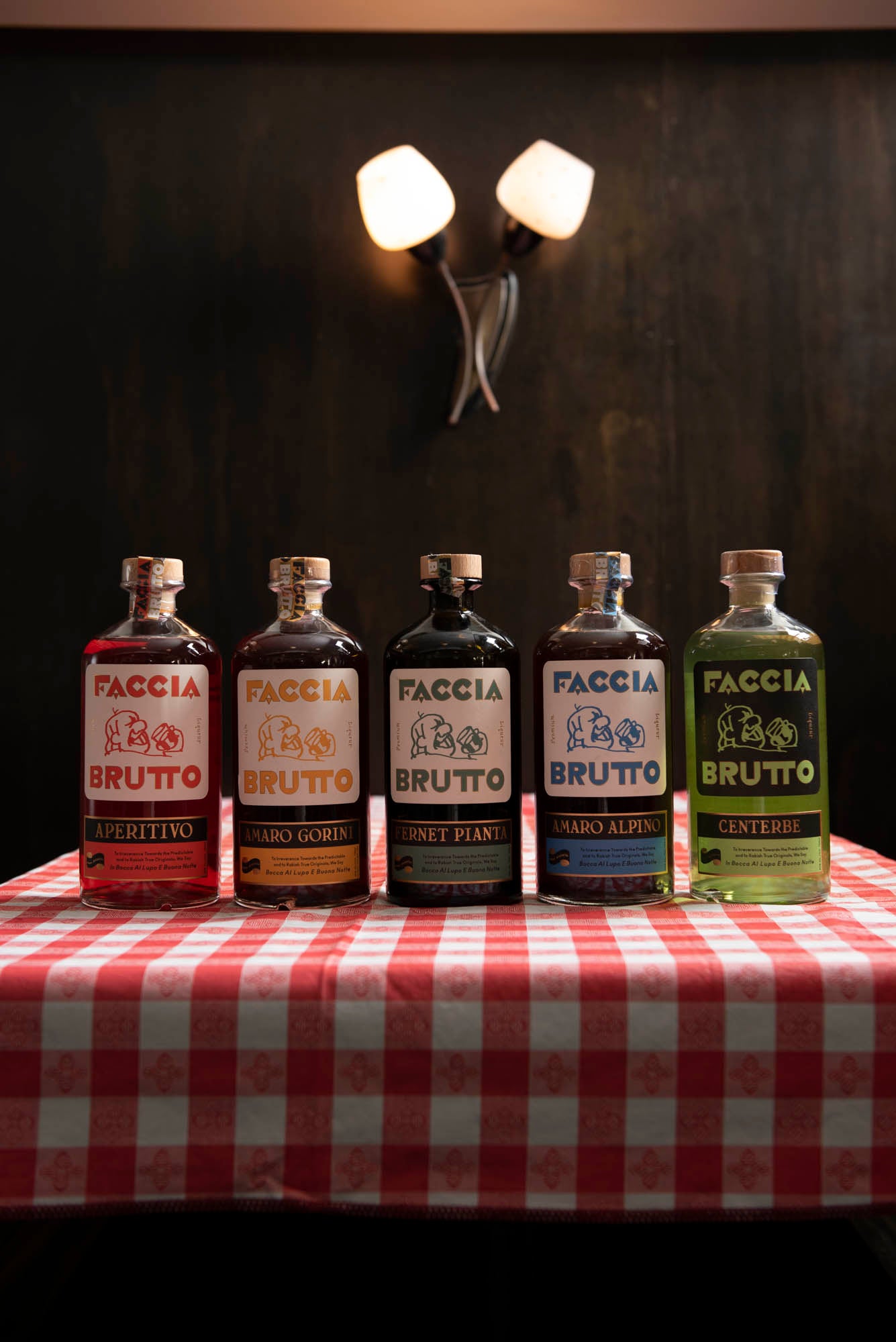 Five Faccia Brutto bottles lined up on table with classic red checkered table cloth