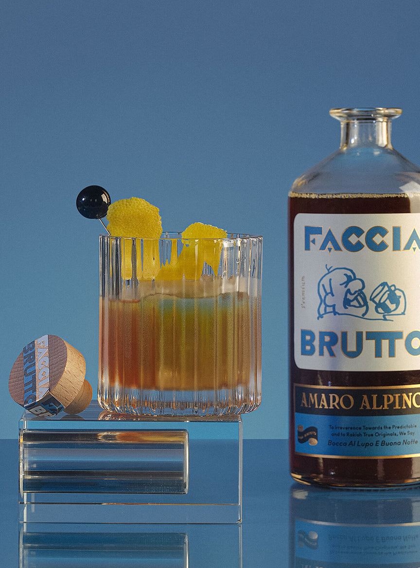 Cocktail glass with Faccia Brutto Amaro Alpino bottle in the background