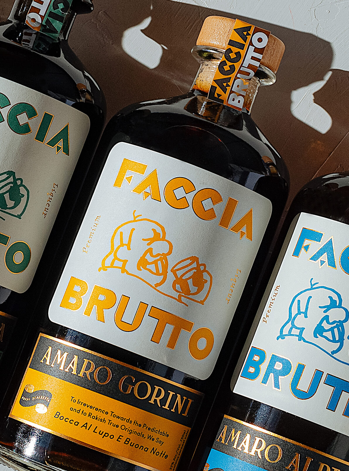 Bottles of Faccia Brutto laid down on white painted background featuring Amaro Gorini