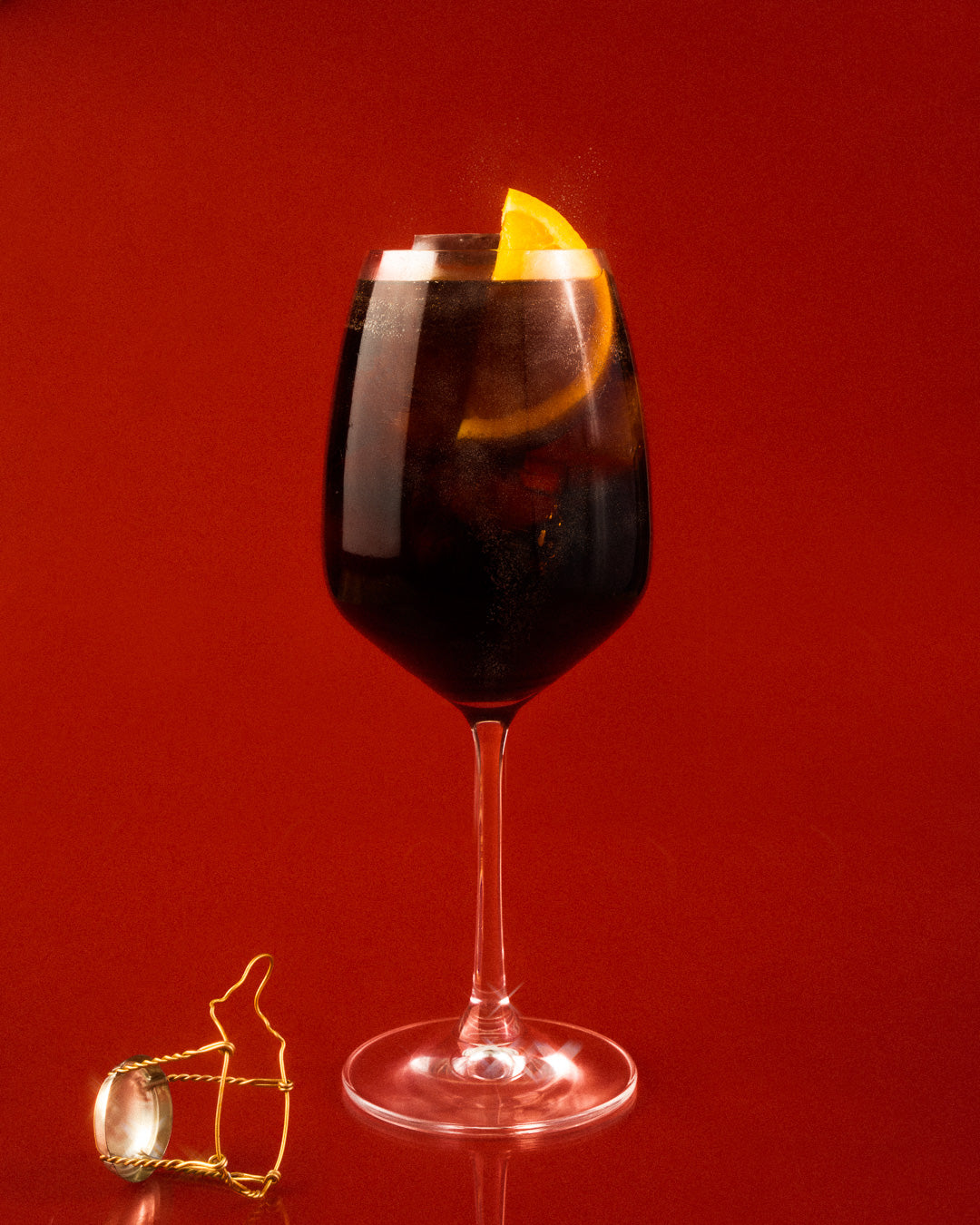 Wine glass full of brown cocktail with orange slice and champagne cork on the side