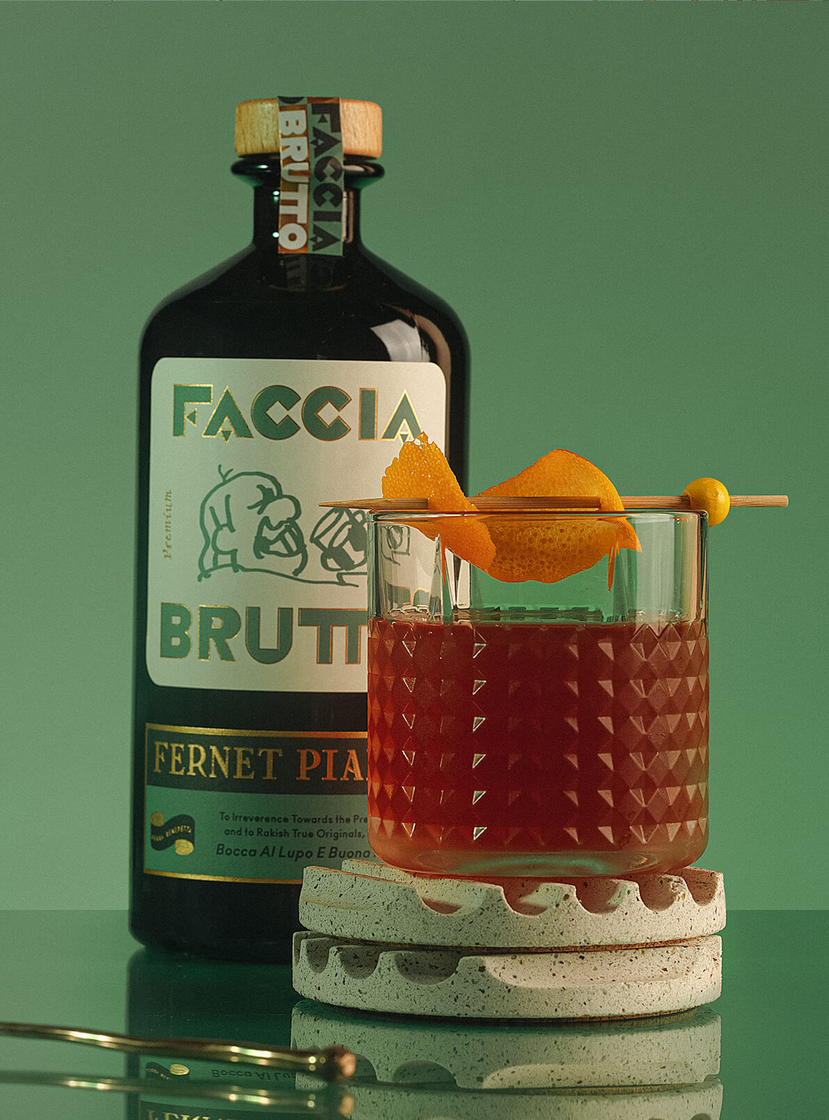Cocktail with orange peel on coaster with Faccia Brutto Fernet Pianta bottle in the background 